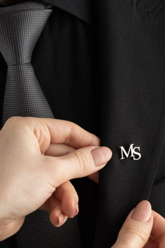 Hand adjusting a suit button with a logo on a black suit jacket.