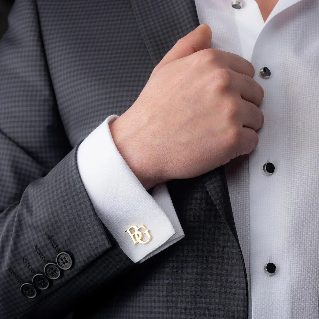 Close-up of a person adjusting a suit jacket with a cufflink on a gray checkered suit and white shirt.