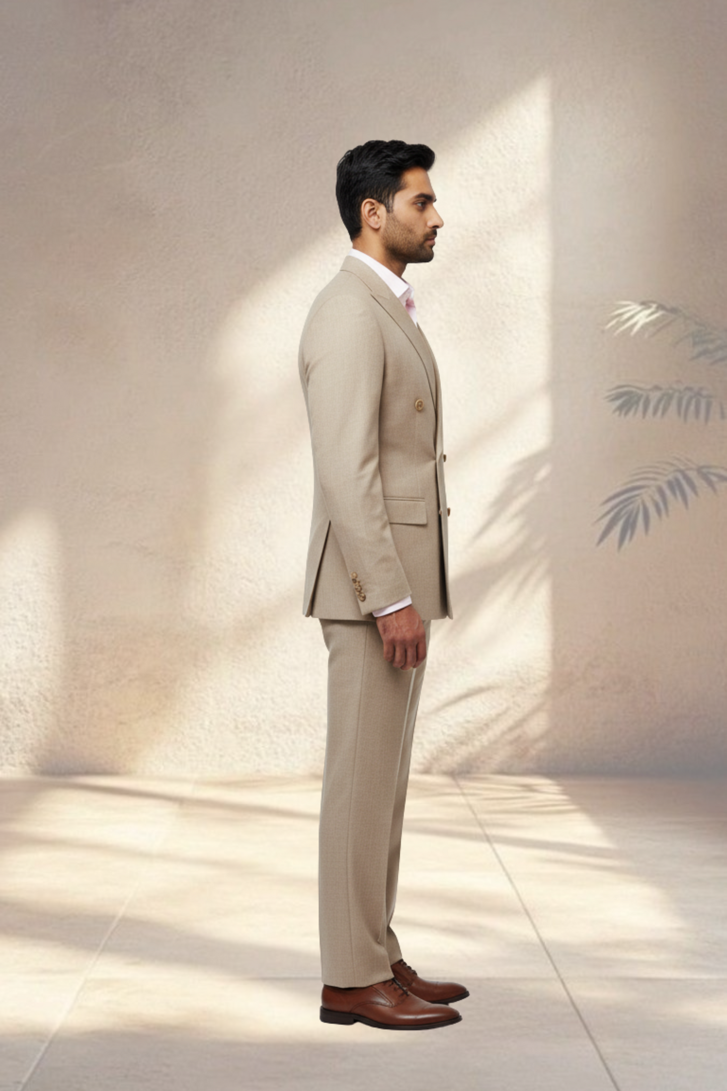 Man wearing a beige suit standing in a softly lit room with a light-colored wall.