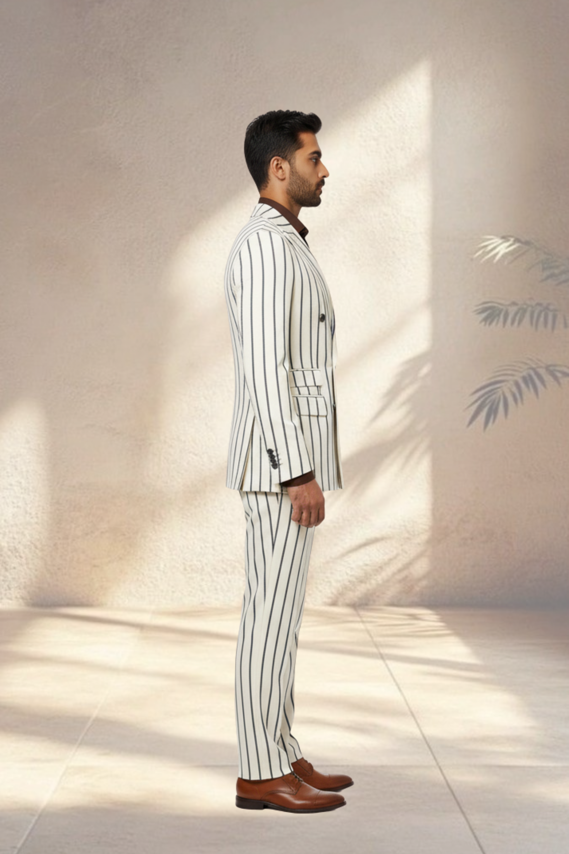 Man wearing a white pinstripe suit with brown shoes standing against a light wall.