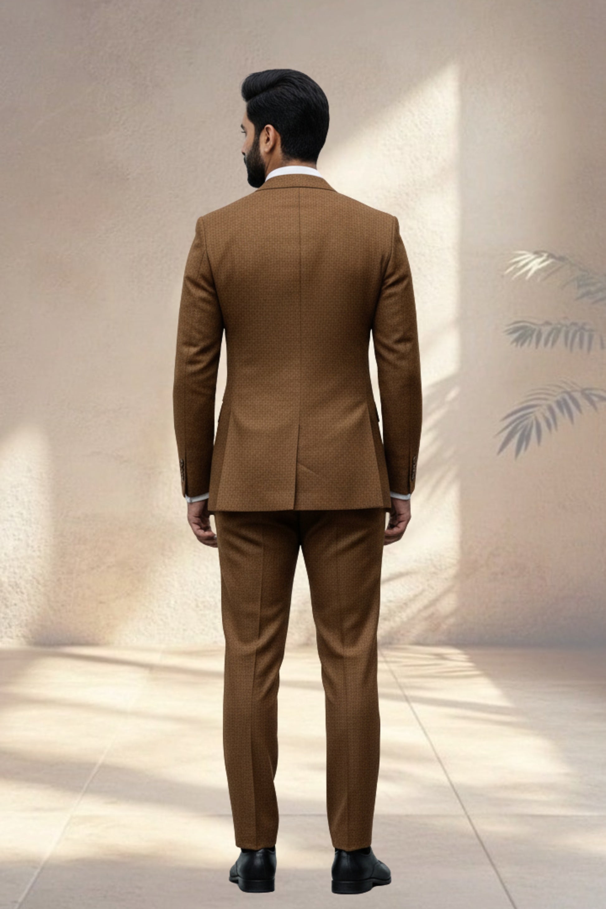Man wearing a brown suit standing against a neutral wall.