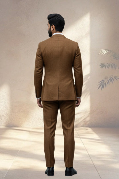 Man wearing a brown suit standing against a neutral wall.