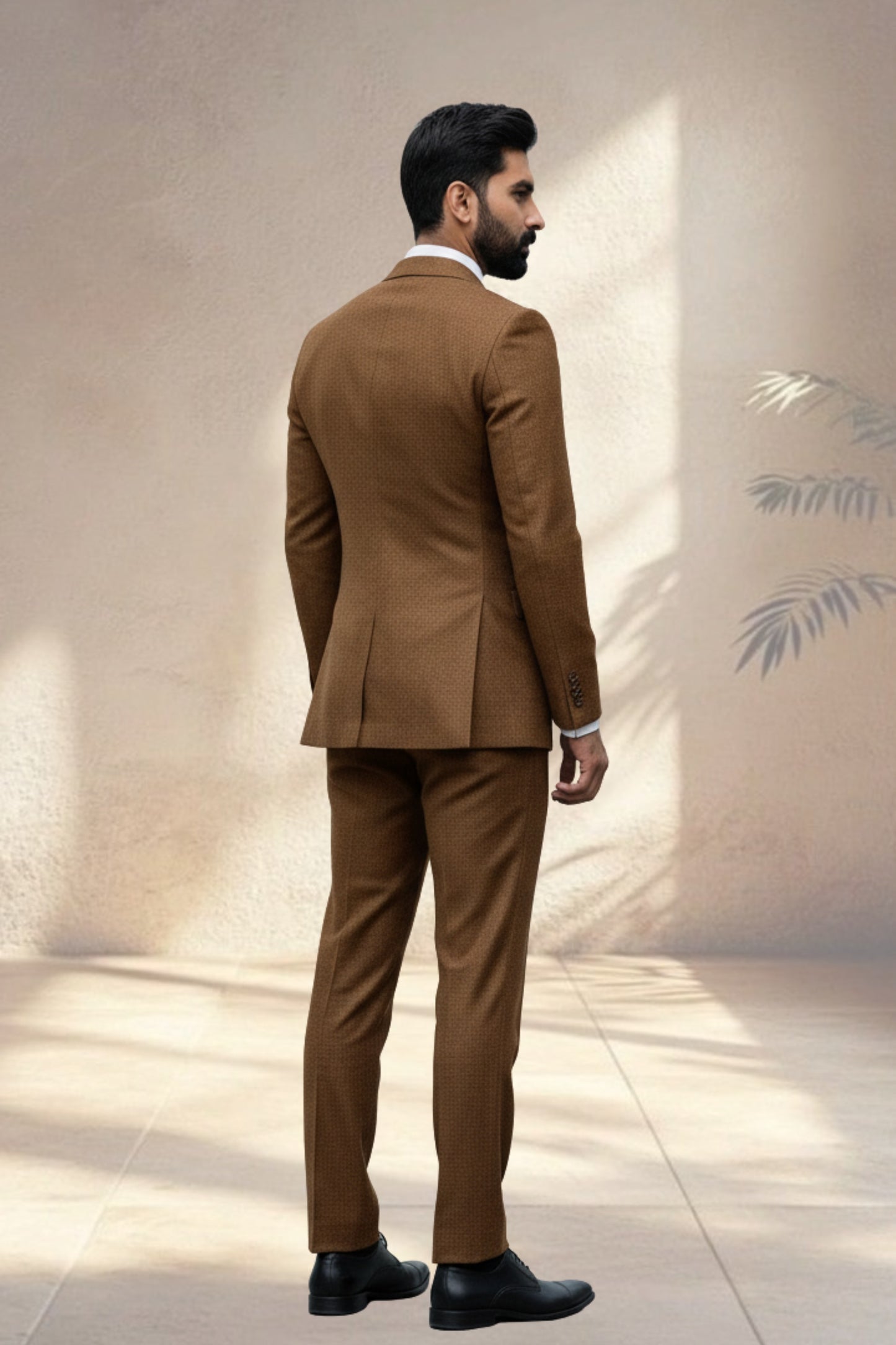 Man wearing a brown suit standing against a neutral wall.