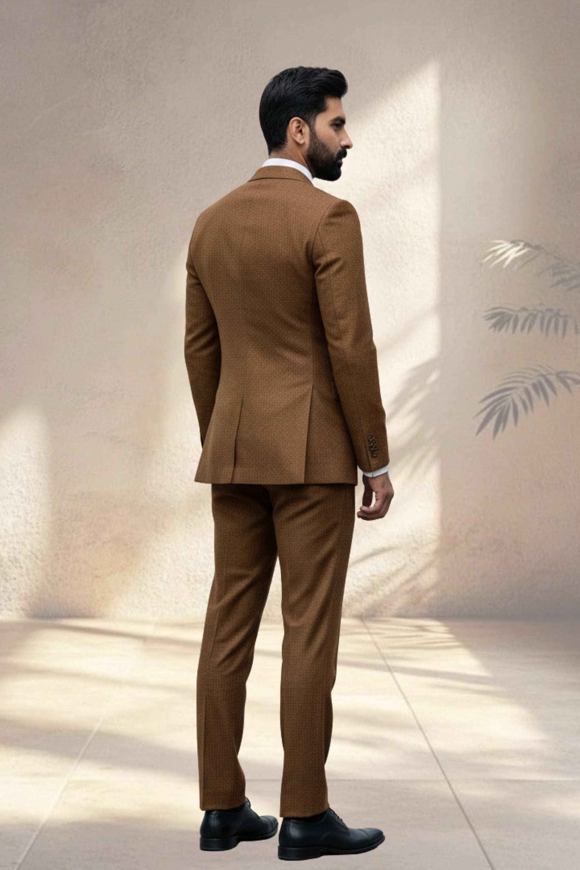 Man wearing a brown suit standing against a neutral wall.