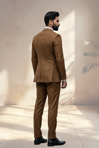 Man wearing a brown suit standing against a neutral wall.
