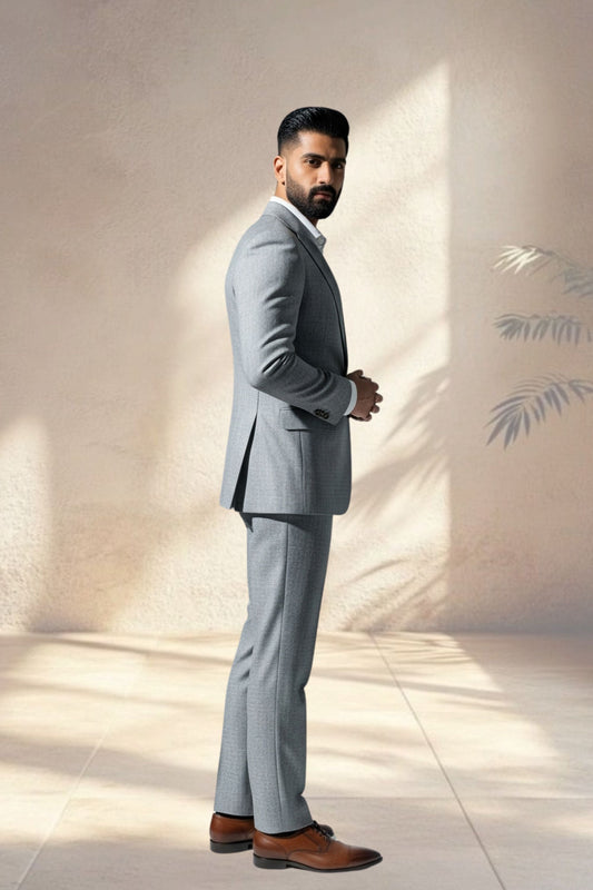 Man wearing a gray suit standing against a light wall with a minimalistic design.